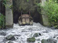 Photo showing water pouring out of a concrete structure with a man-hole cover.