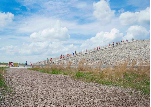 A group of people in a line, walking down the large disposal cell. Plants surround the feature.