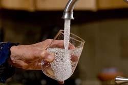 A hand putting a glass under a faucet and filling it with water.