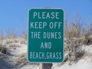 Warning sign near beach sand dunes. Sign text: “Please keep off the dunes and beach grass”