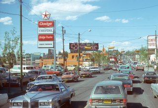 Traffic along a major road. Cars appear to be from the mid to late 20th century.