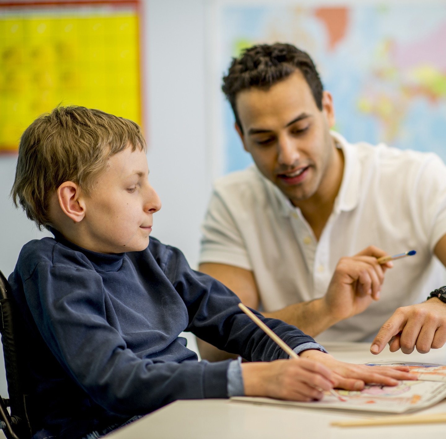 child in wheelchair working with teacher in school setting