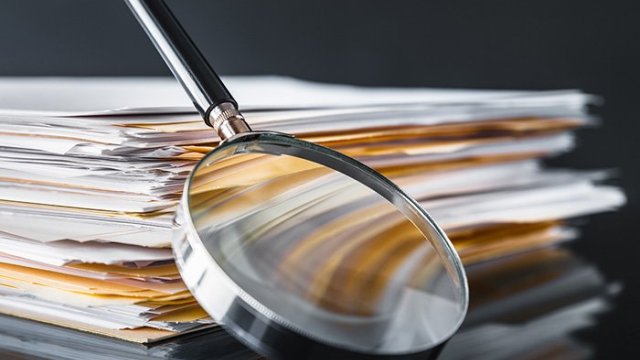 A stack of folders full of documents with a magnifying glass leaning up against the stack.