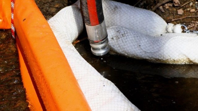 Vacuum trucks are placed near booms to collect oil sheen generated during stream and culvert cleanup