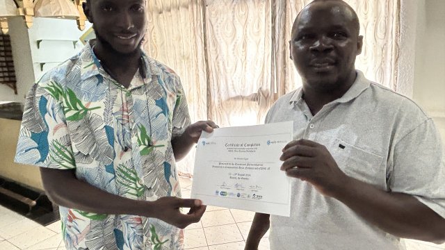 Man wearing floral shirt smiling at camera and receiving a certificate of completion from man wearing white polo top.