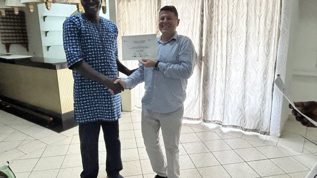 Man wearing blue shirt smiling at camera and receiving a certificate of completion from man wearing sky blue shirt.