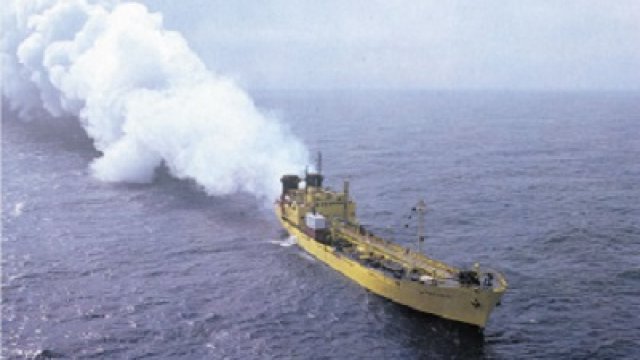 vessel on the ocean incinerating waste at sea with a large cloud of smoke trailing behind the vessel