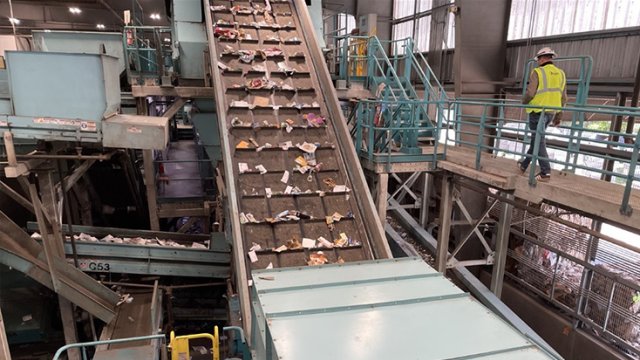 the inside of a materials recovery facility looking at a man walking on the platforms between sorting conveyer belts