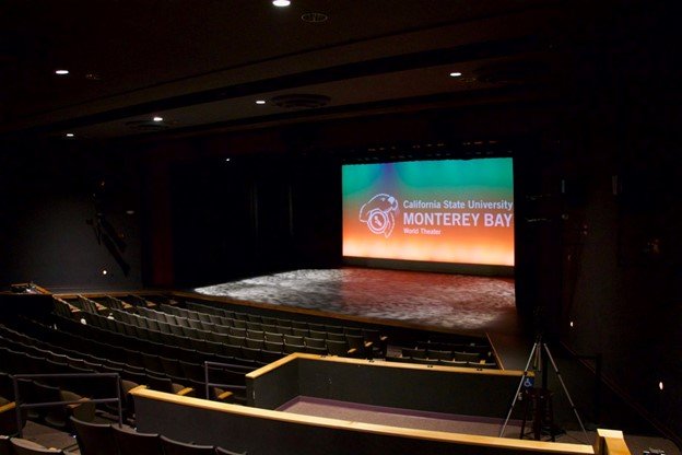 Inside of a theater with a screen reading 'California State University Monterey Bay World Theater'