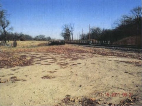 A dirt field and blue sky with trees in the background