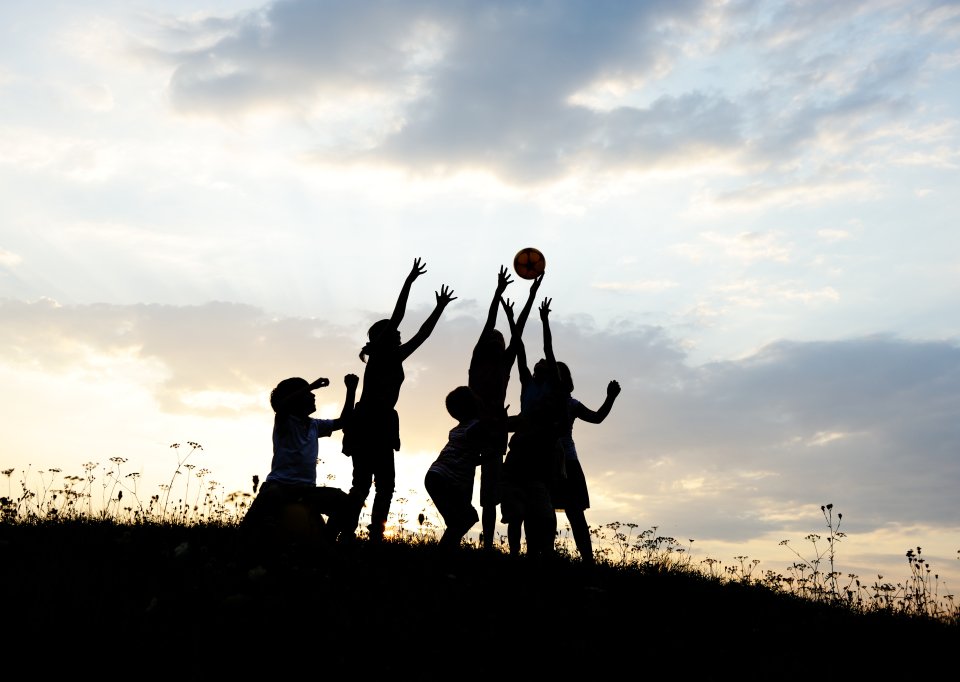 Group of children reach for a ball in unison at the crest of a hill