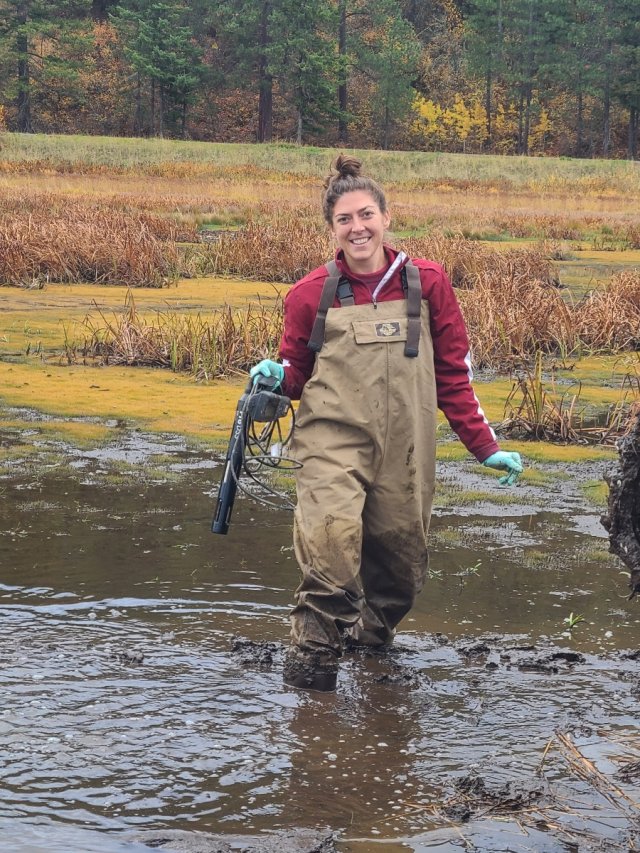 Amy Rice standing in knee-deep water holding measurement equipment.