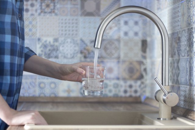 Person holding cup under water faucet.