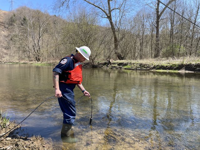 Individual in the stream with scientific instruments monotiring the water