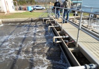 While standing above an aeration basin the compliance advisor discusses operations with the wastewater system operator.