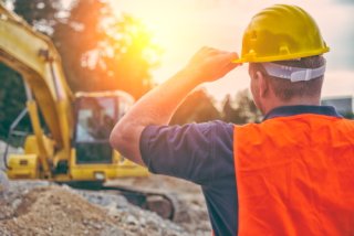 A worker wearing PPE and facing away from the camera looks on at a construction site.