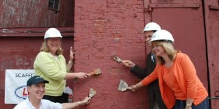 Project staff posing with paint scrapers at an exterior wall of the Tarr and Wonson Paint Manufactory in Gloucester, MA.