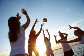 Group of young adults playing volleyball on a beach.