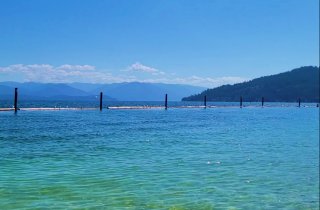 Lake of blue water with logs lined up a short distance out on the surface of the water for a swimming area and mountains in the background.