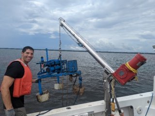 Researcher stands on boat next to water testing equipment wearing a life jacket