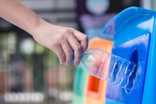 This is a photo of a person putting a plastic bottle into a recycling bin