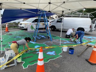 Three people painting a large mural of the Mystic River Watershed on the ground