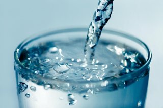 Half of a glass cup being filled with tap water.