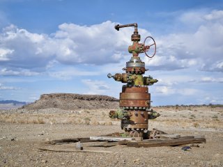 Abandoned wellhead pictured in the middle of the desert with sky in the background