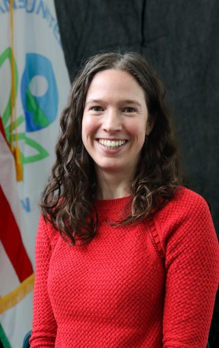 EPA scientist Emma D'Ambro posing for a smiling headshot in front of the epa flag