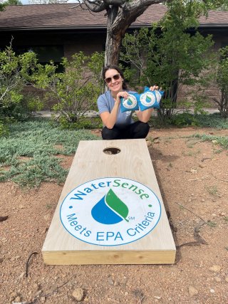 Photo of a women kneeling behind a cornhole board with a WaterSense label on it