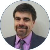 Speaker Ken Yale has dark hair and beard and is wearing a dark suit with a lavender button down shirt and tie while standing against a white background.